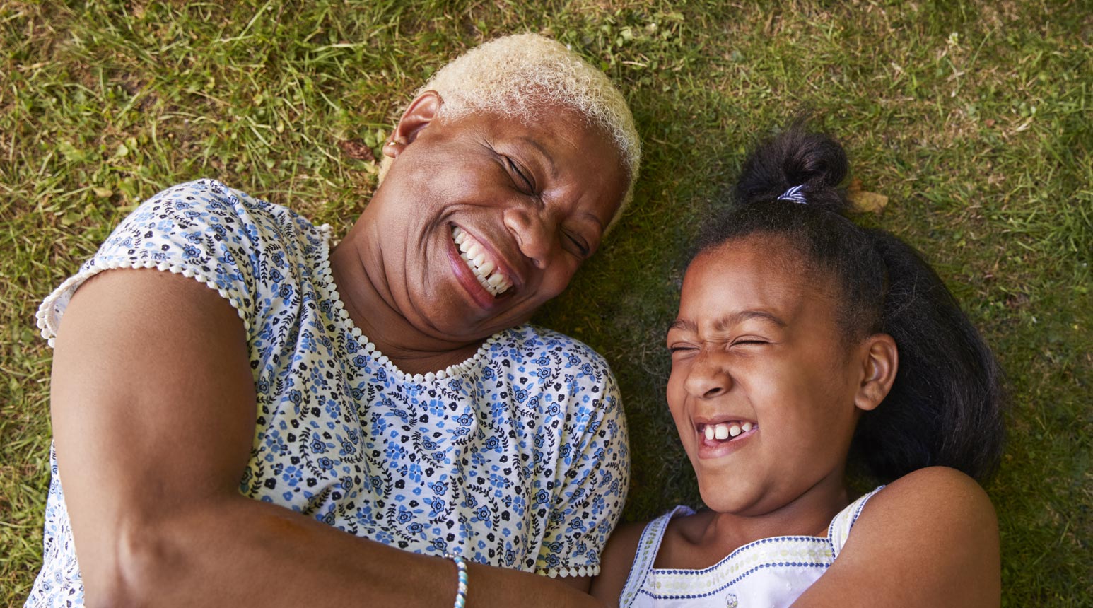 About us 1 Grandmother and granddaughter laughing in the grass.